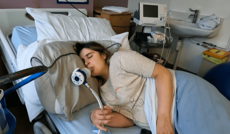 Woman in hospital bed using breathing apparatus.