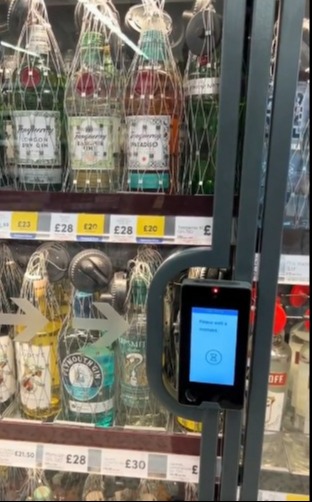 Liquor bottles in a secured display case with a digital payment terminal.