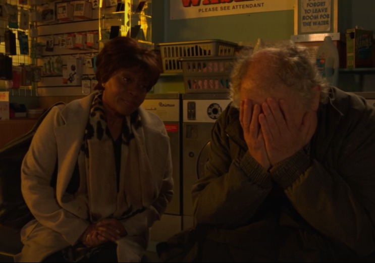 A woman sits beside a distressed man in a laundromat.