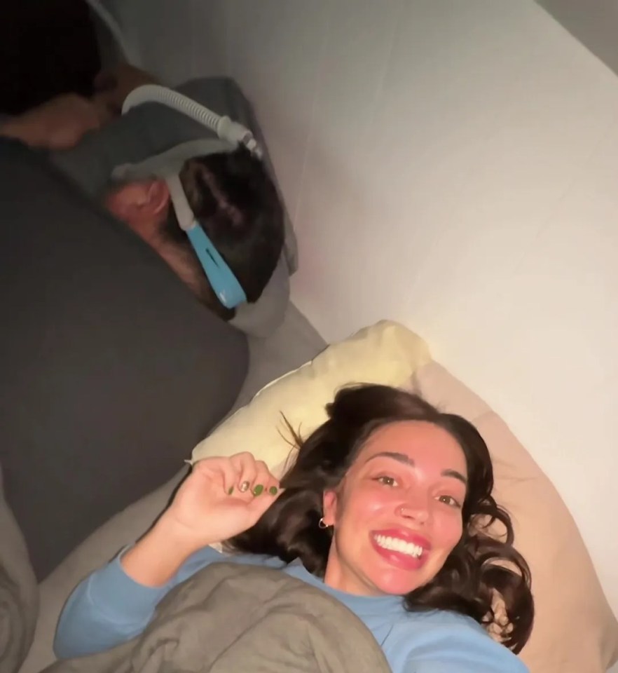 A young woman in bed with a 52-year-old man using a CPAP machine.