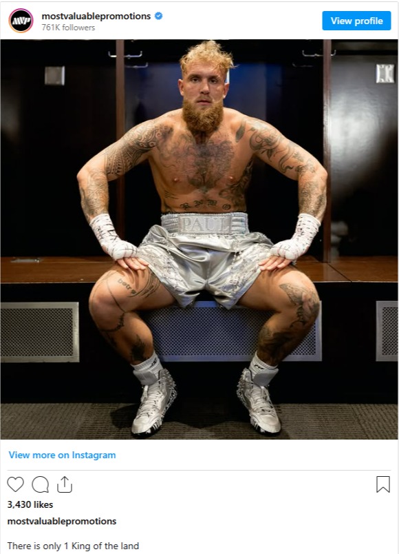 A tattooed boxer in silver boxing shorts sits in a locker room.