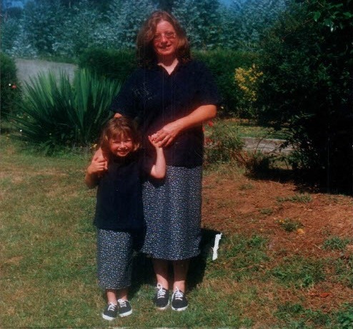 A mother and daughter stand together outdoors.