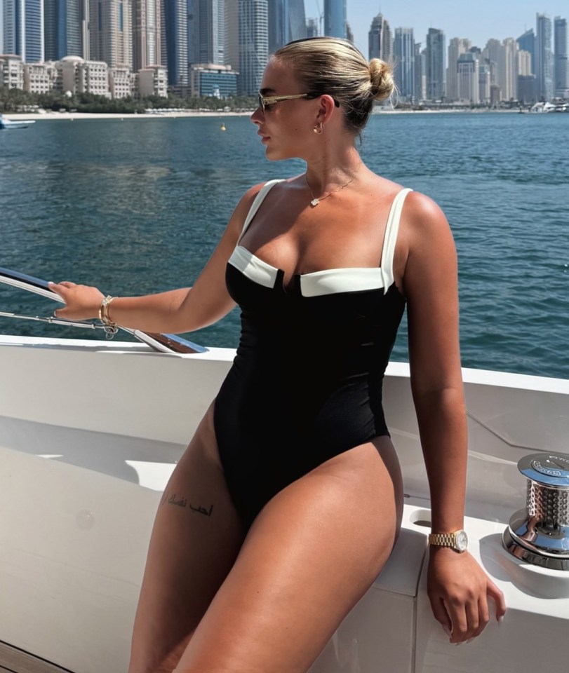 Woman in a swimsuit on a yacht with Dubai skyline in the background.