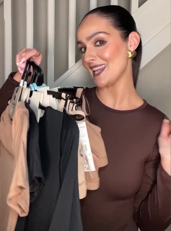 Woman holding up several items of clothing on hangers.