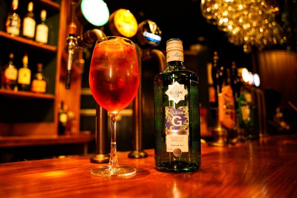 A non-alcoholic drink in a stemmed glass and a bottle of Clean G alcohol-free spirit on a bar.