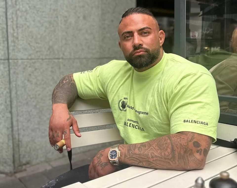 Saman Baghi, a bodybuilder, sits at a table outdoors.