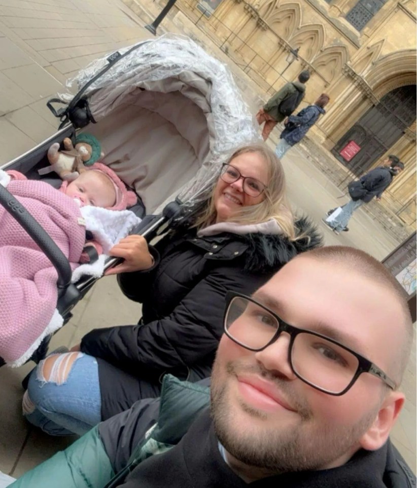 A man, woman, and baby in a stroller in front of a cathedral.