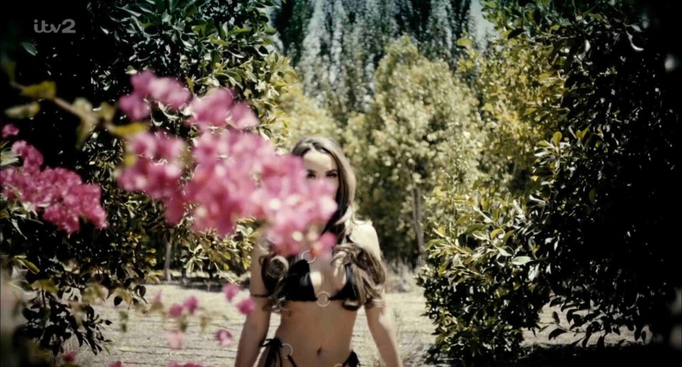 Woman in bikini walking through a garden.