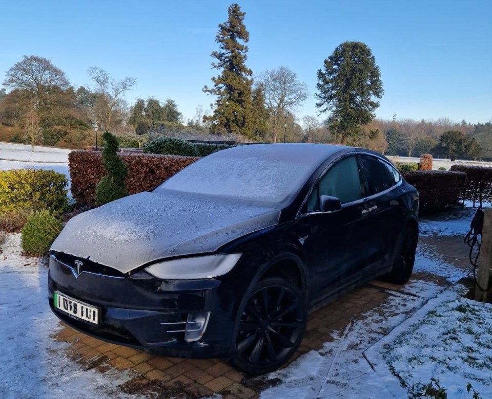 Snow-covered Tesla Model X parked in a driveway.