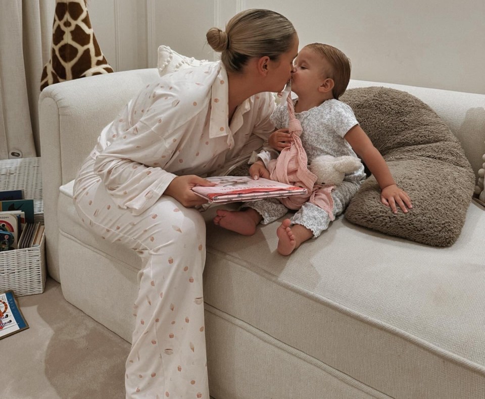 Woman kissing baby while reading a book.