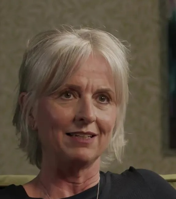 Woman speaking, wearing a black shirt and butterfly necklace.