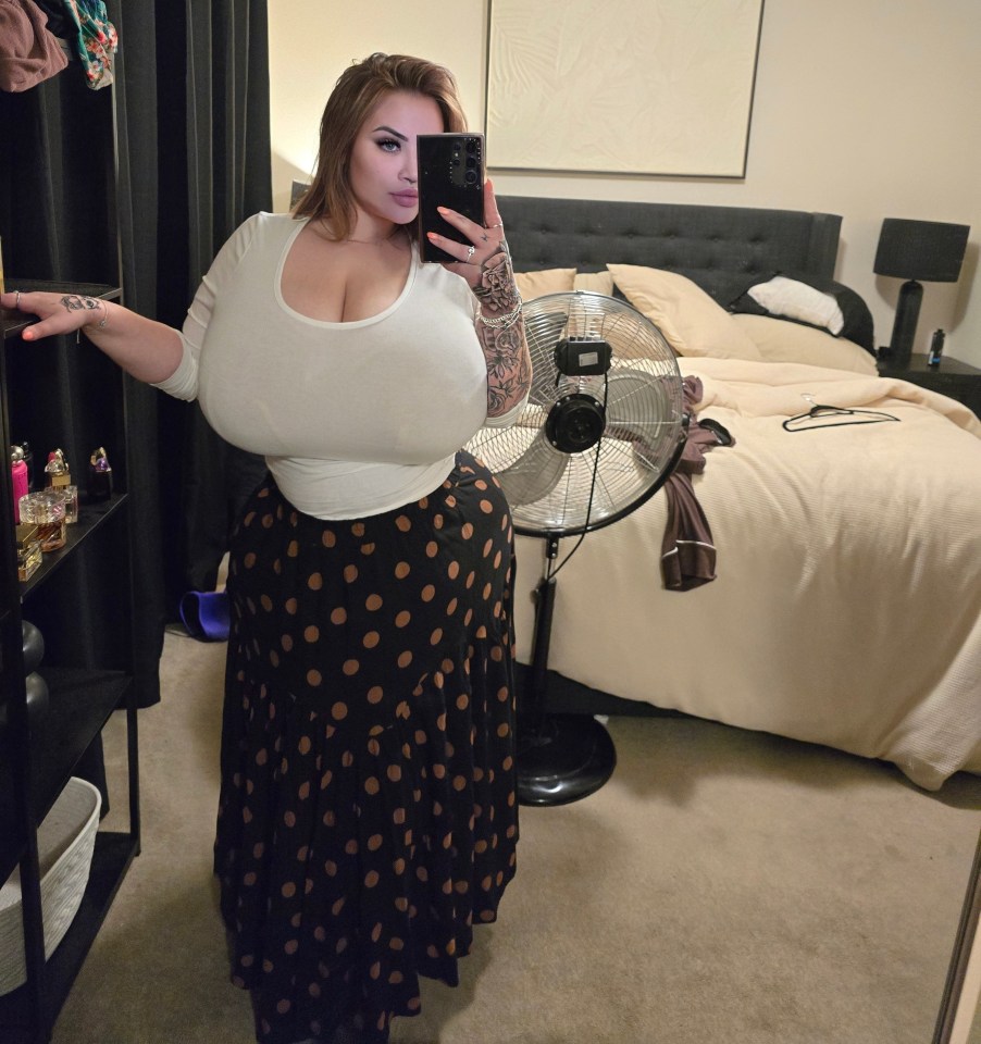 Woman with large breasts takes a selfie in her bedroom.