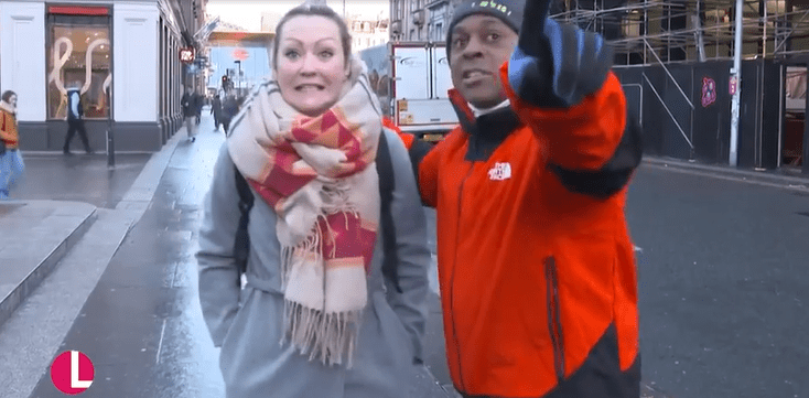 A man and a woman on a city street; the man is pointing.