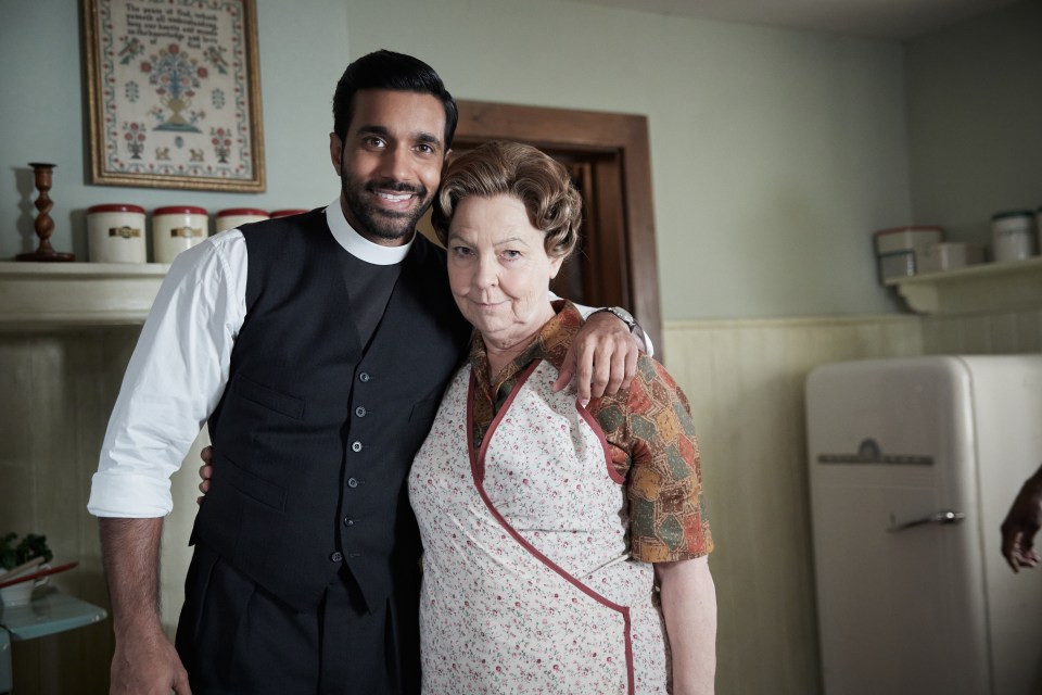 A priest and an older woman embracing in a kitchen.