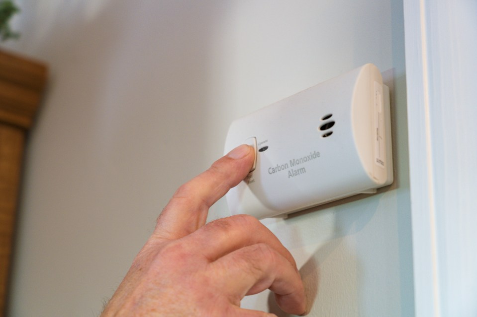 A hand punching a test button on an electrical Carbon Monoxide Alarm