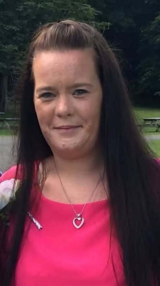 Portrait of a woman with long dark hair wearing a pink top and heart necklace.