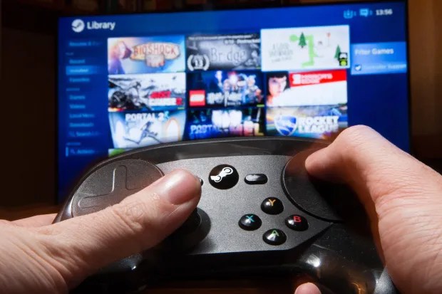 Hands holding a Steam Controller in front of a Steam game library on a TV screen.