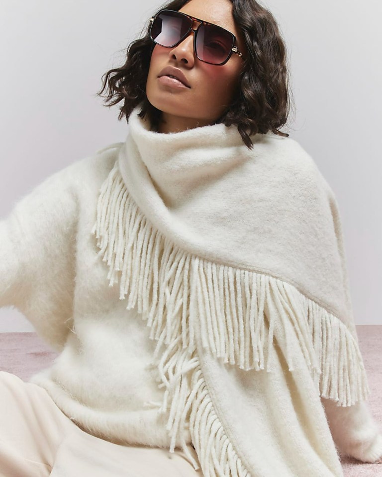 Woman wearing a fringed cream sweater and sunglasses.