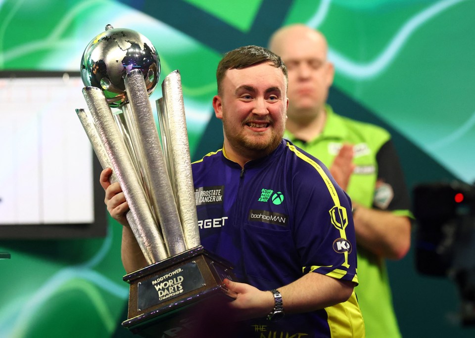 Luke Littler holding the World Darts Championship trophy.