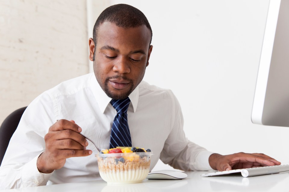 Businessman eating yogurt and granola with fruit at his desk.