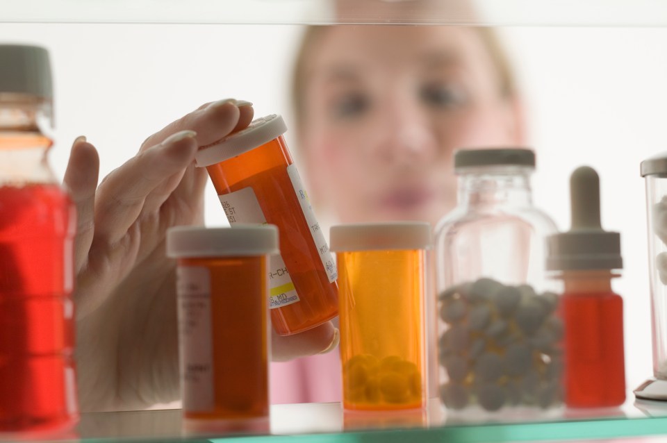 Woman's hand taking prescription medication from medicine cabinet.