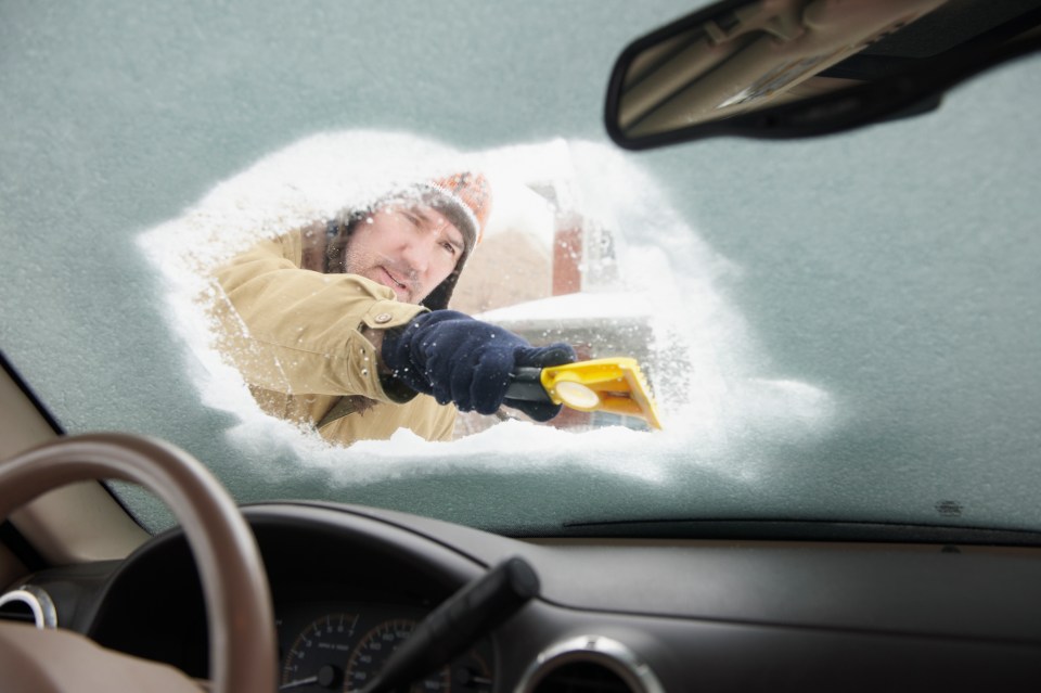 Man scraping snow from his car windshield.