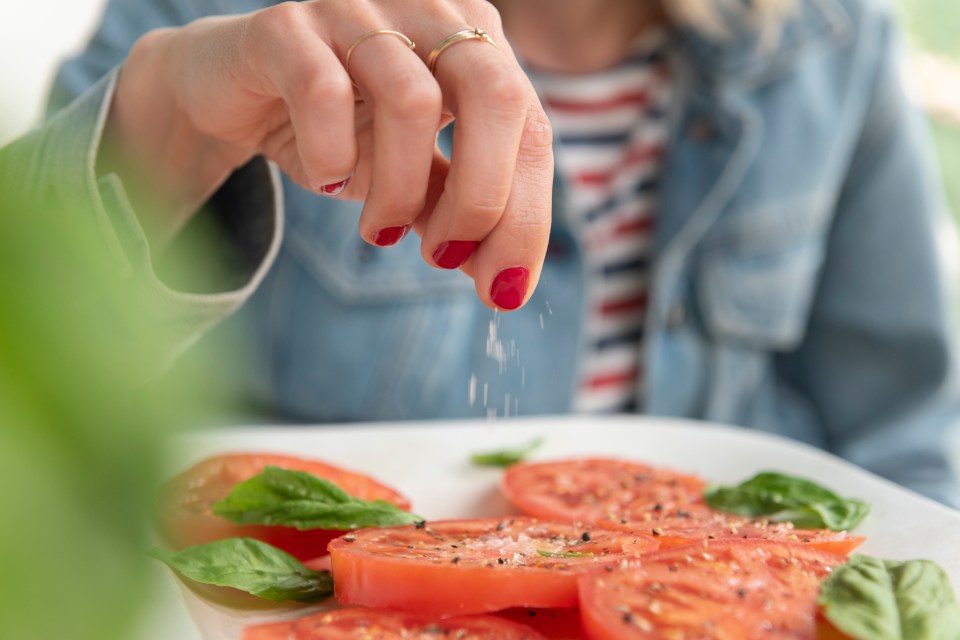 Woman sprinkling salt on sliced tomatoes and basil.