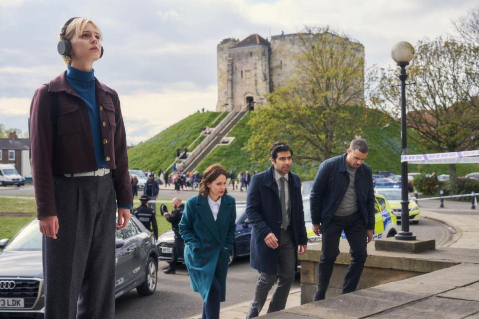 Four detectives investigate a crime scene near a castle.