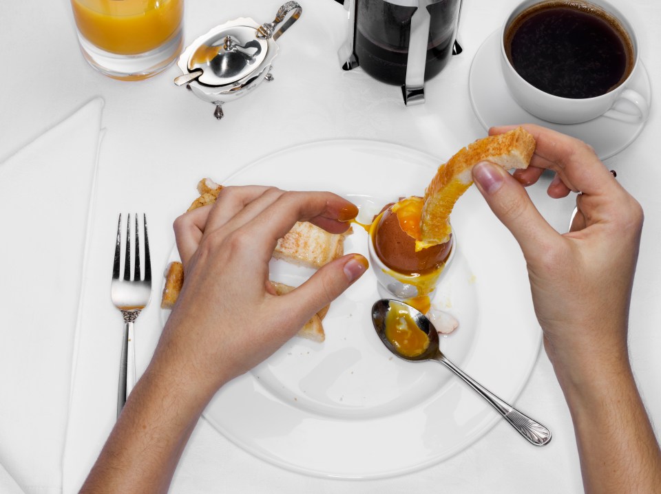 Person dipping toast into a soft-boiled egg for breakfast.