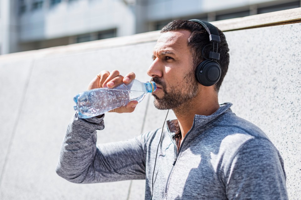 Man in headphones drinking water from a plastic bottle.