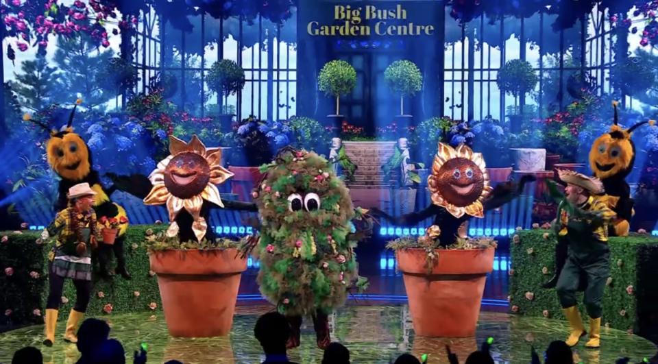 The Masked Singer: Bush costume in a garden setting with other plant costumes.