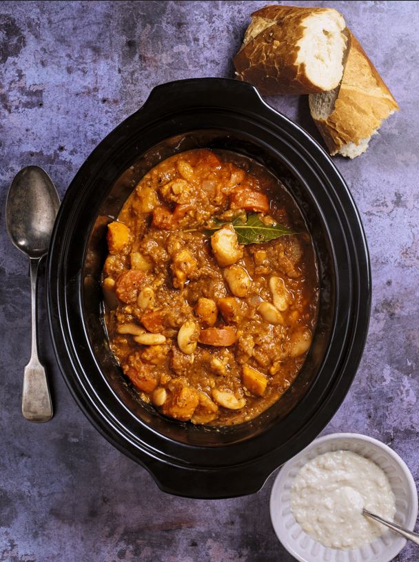 Sunshine stew in a slow cooker with bread and a side of creamy sauce.