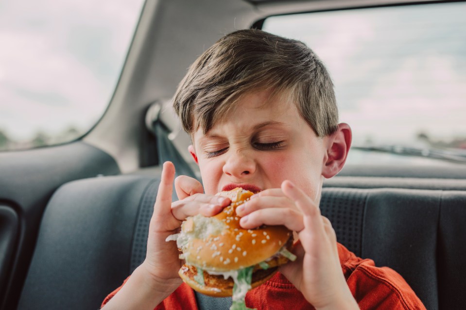 Boy eating a hamburger in a car.