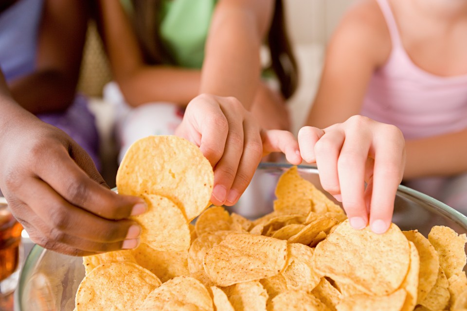 Three girls reaching into a bowl of tortilla chips.