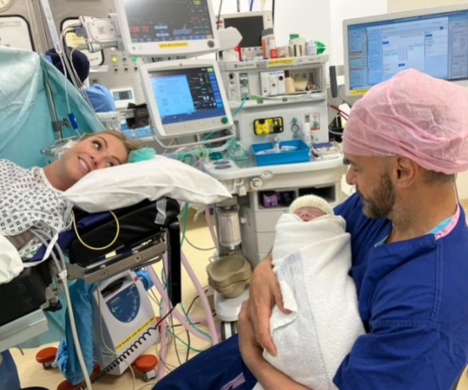 A woman in a hospital bed, a man holding a newborn baby.