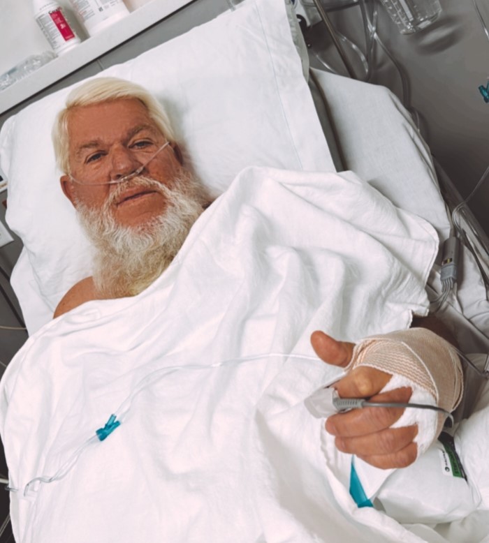 Man in hospital bed with nasal cannula and bandaged hand.