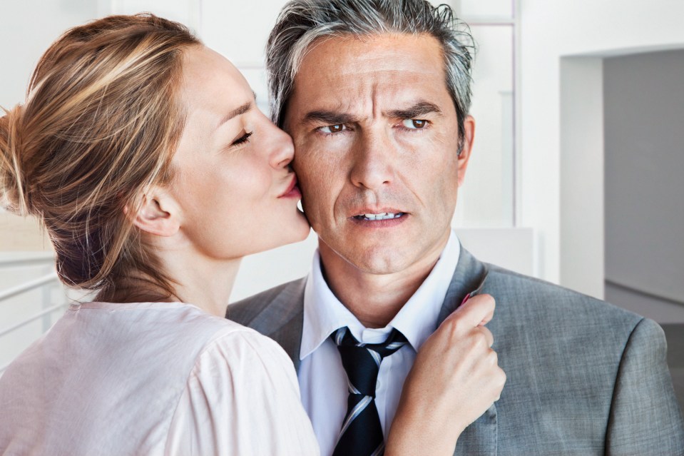 A woman kisses a man's cheek while he looks displeased.