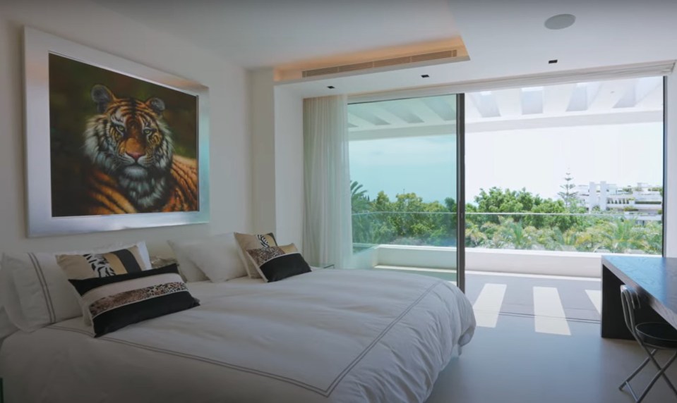 Bedroom with large window overlooking a balcony and trees.  A large framed tiger painting is on the wall.