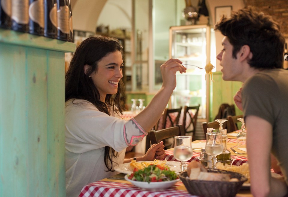 A young woman feeds her date pasta at an Italian restaurant.