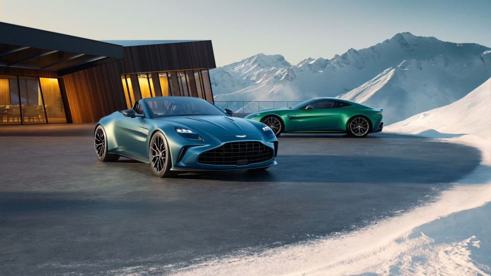 Two Aston Martin Vantage Roadsters parked outside a modern building in a snowy mountain setting.