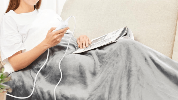 Person using an electric blanket while reading a magazine.