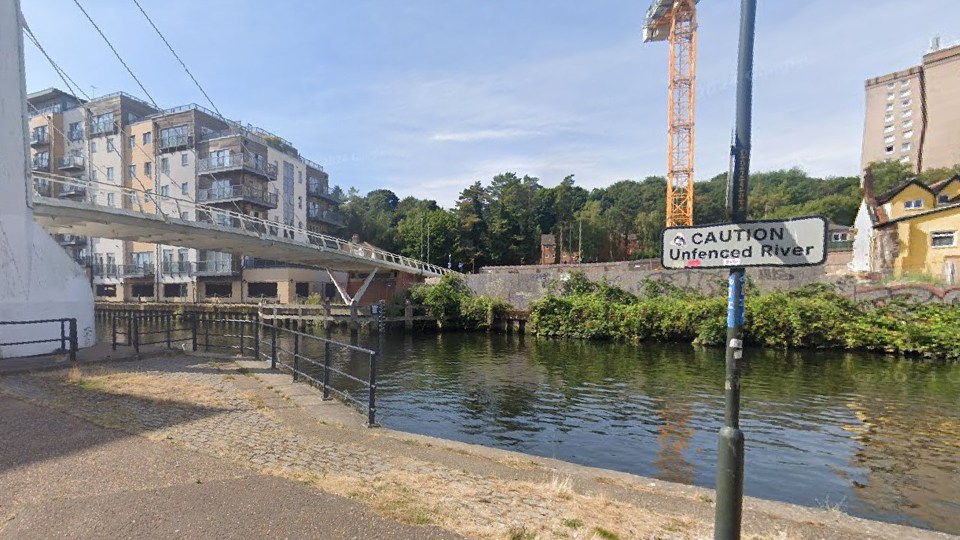 Caution: Unfenced river by footbridge and apartment building.