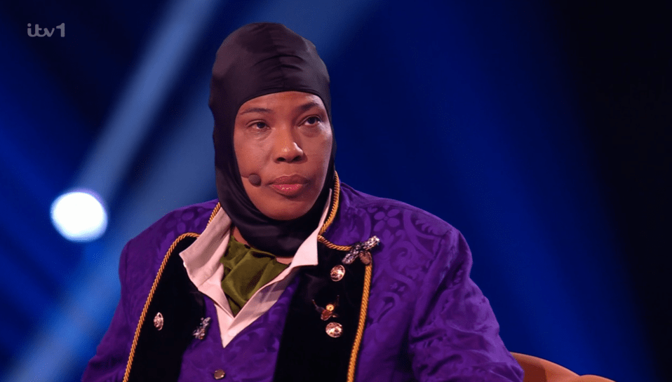 Screenshot of a woman wearing a purple jacket and black balaclava.