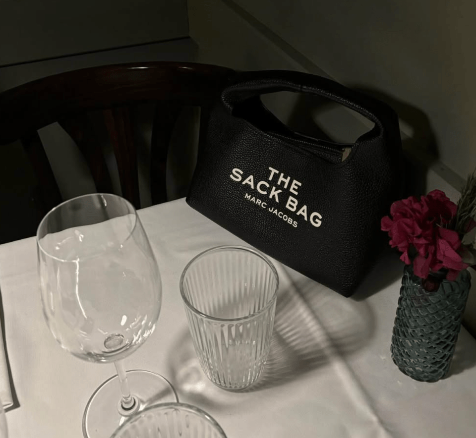 Marc Jacobs "The Sack Bag" on a table with wine glasses and a vase of flowers.