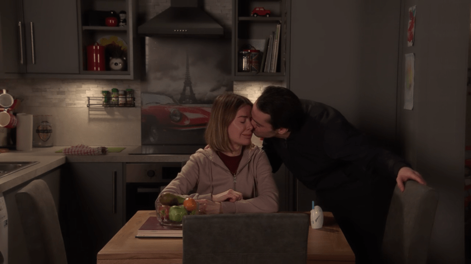 A man kissing a woman on the forehead in a kitchen.