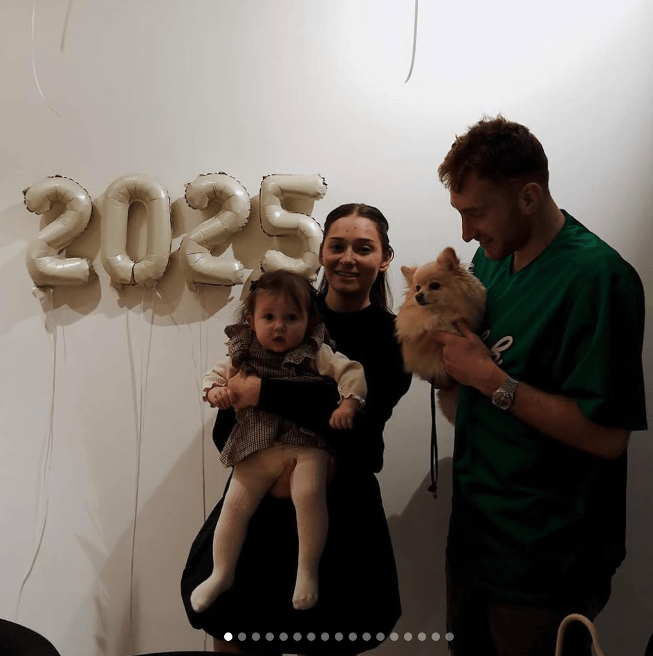 Family with baby and dog in front of 2025 balloons.