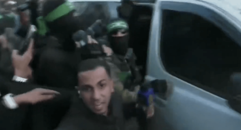 Screenshot of a chaotic scene with people in dark clothing and green headbands near a van.