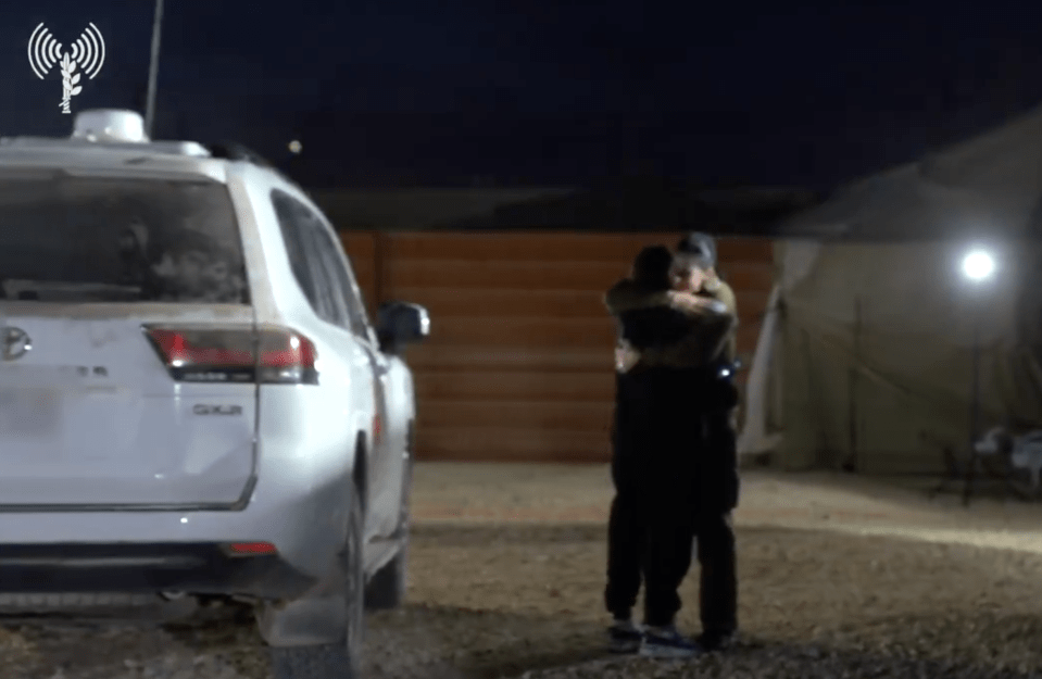 Two people embracing at night near a vehicle.