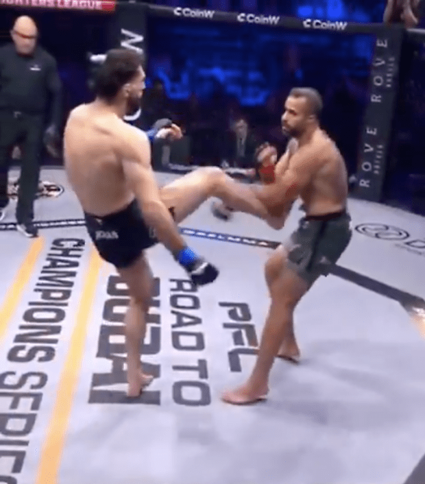 Two MMA fighters in a match. One fighter throws a kick.