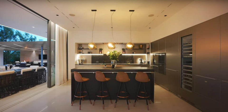 Modern kitchen island with four bar stools and a view of a patio through large glass doors.